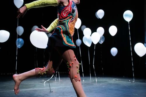 Eine Artistin in bunten Kleidern inmitten von Luftballons