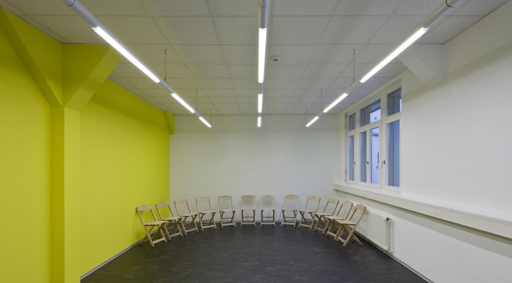 Sitzungszimmer mit dunklem Boden und gelber Wand, rechts ein Fenster