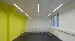 Sitzungszimmer mit dunklem Boden und gelber Wand, rechts ein Fenster